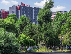 Un bĂątiment dâhĂŽtel moderne, avec une enseigne « IBIS HOTEL » bien visible, entourĂ© dâune vĂ©gĂ©tation luxuriante et de voitures garĂ©es.