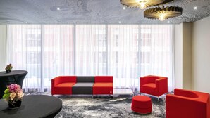 A modern room with a large window, a sofa, two red chairs, a round table, and a unique ceiling design. - ibis Bucharest Politehnica (Bucharest)