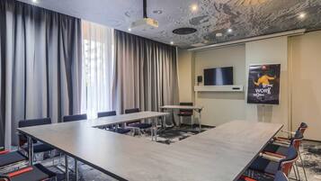 A conference room with a long table, chairs, a TV, and a poster.