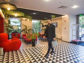 Um interior moderno com um chão estampado em padrões geométricos, assentos vermelhos e plantas em vasos.