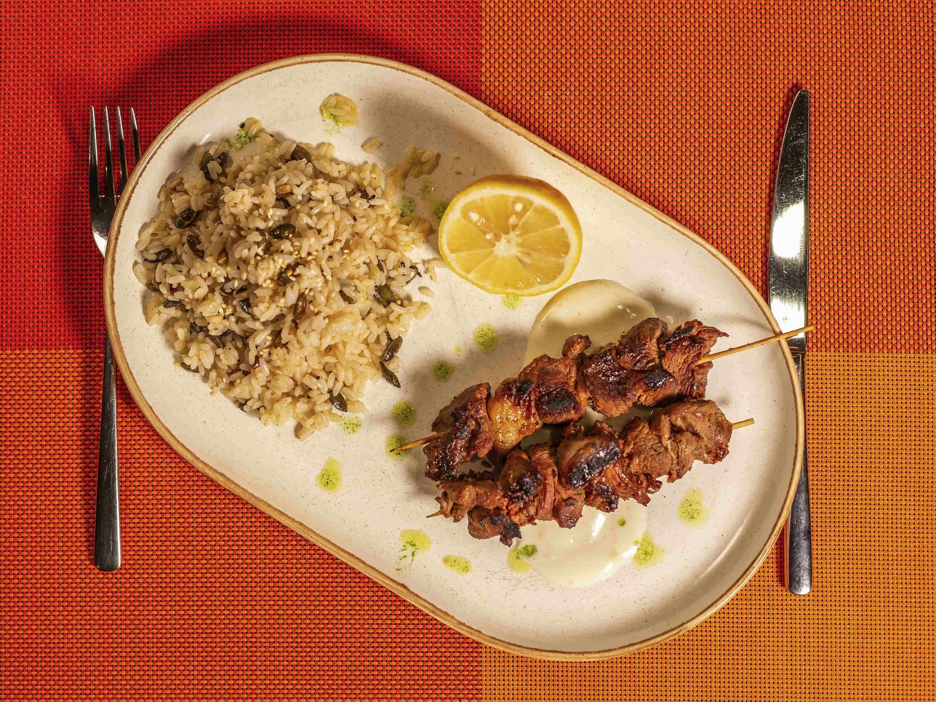 A plate with rice, lemon, and skewered meat.