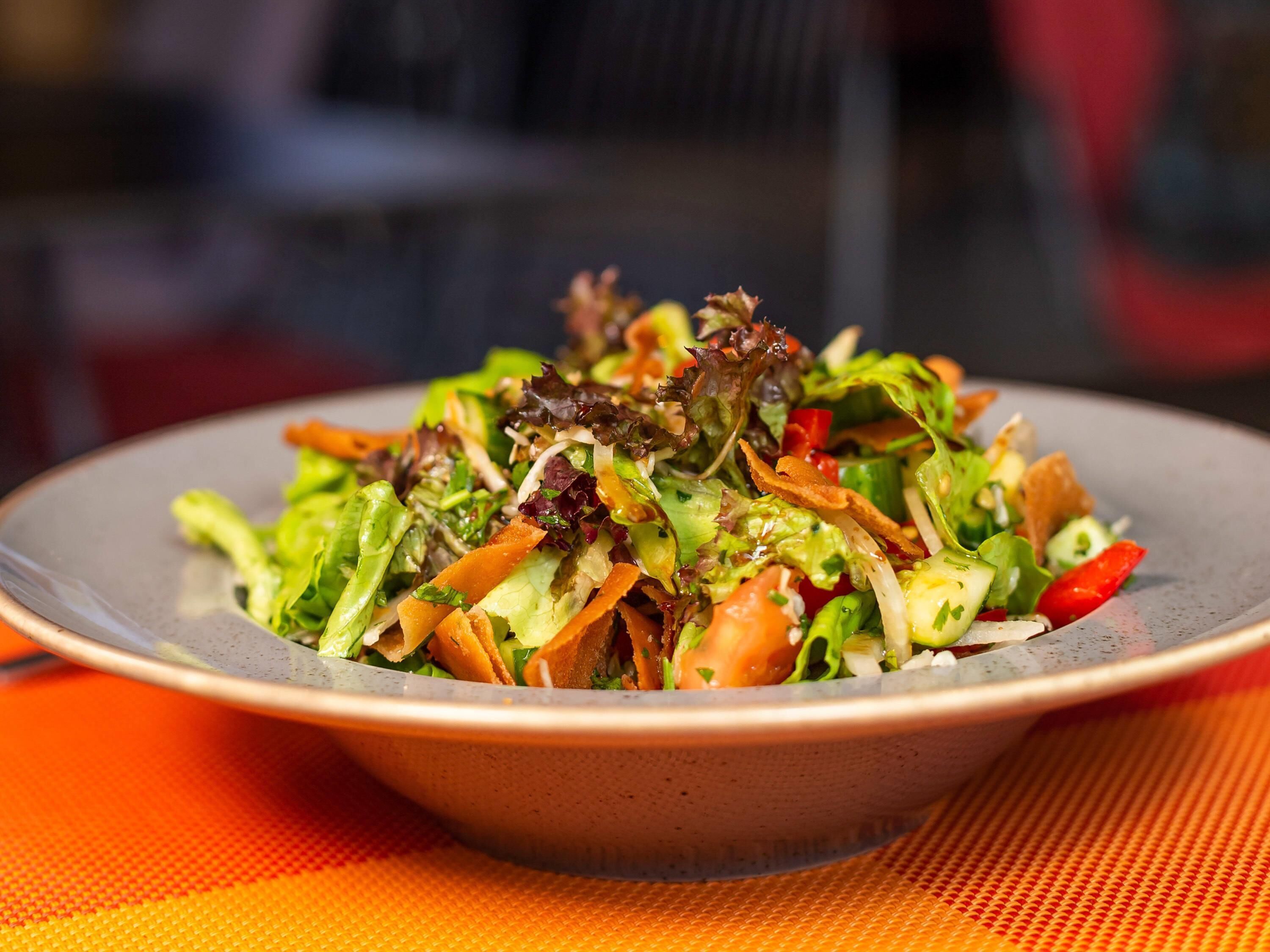 Een saladekom met verschillende groenten en bladgroenten op een bord.