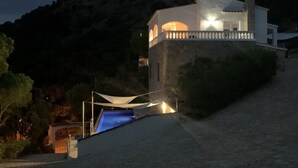 Ein modernes Gebäude mit Schwimmbad, umgeben von einem pflasterbelagten Bereich und einem Berg im Hintergrund.