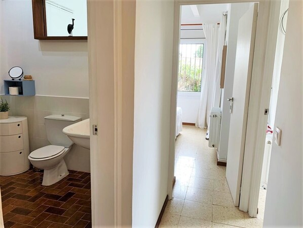 A bathroom with a toilet, sink, and mirror. A hallway leads to a room with a radiator and a window. - Holiday house in a unique quiet location - sea view - private pool - Internet (Roses , Mas Fumats)