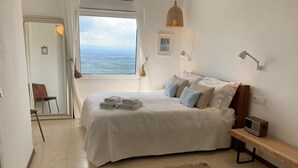 A bedroom with a large bed, a bedside table with a radio, a view of the sea through a window, and a chair in the corner. - Holiday house in a unique quiet location - sea view - private pool - Internet (Roses , Mas Fumats)