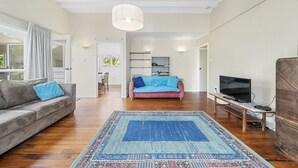 Een ruime woonkamer met een grijze bank, een blauwe en rode bank, een houten salontafel, een televisie en een kamerkleed met een patroon.