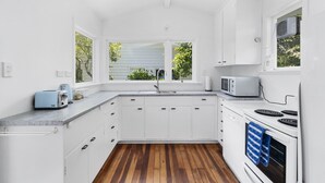 Een moderne keuken met witte kastjes, een houten vloer, een magnetron, een broodrooster en een raam met uitzicht op groen.