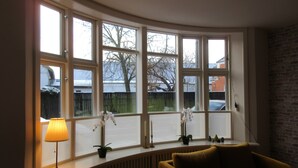 Een kamer met een erker, een radiator, een lamp, een plant en een bank.