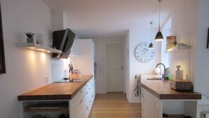 Een moderne keuken met houten aanrechtbladen, witte kastjes en een wandklok.