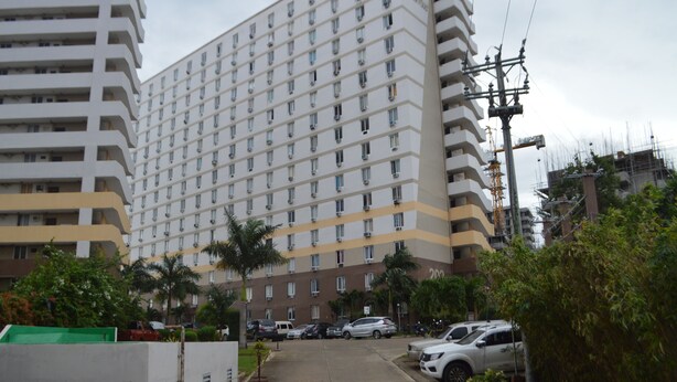 A multi-story hotel with a uniform facade, a parking area with cars, and surrounding greenery. - Dencio's Crib (Lapu-Lapu City)