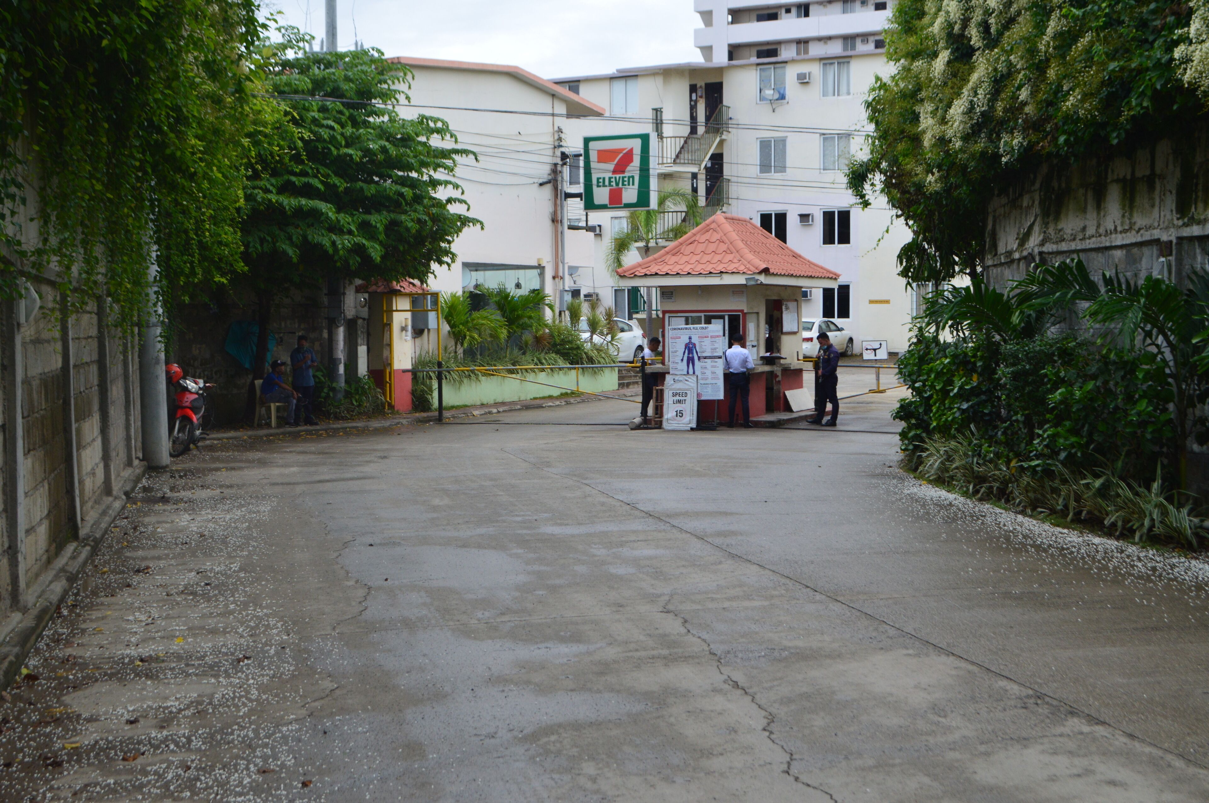 A 7-Eleven convenience store with a red-roofed kiosk, surrounded by buildings and greenery.