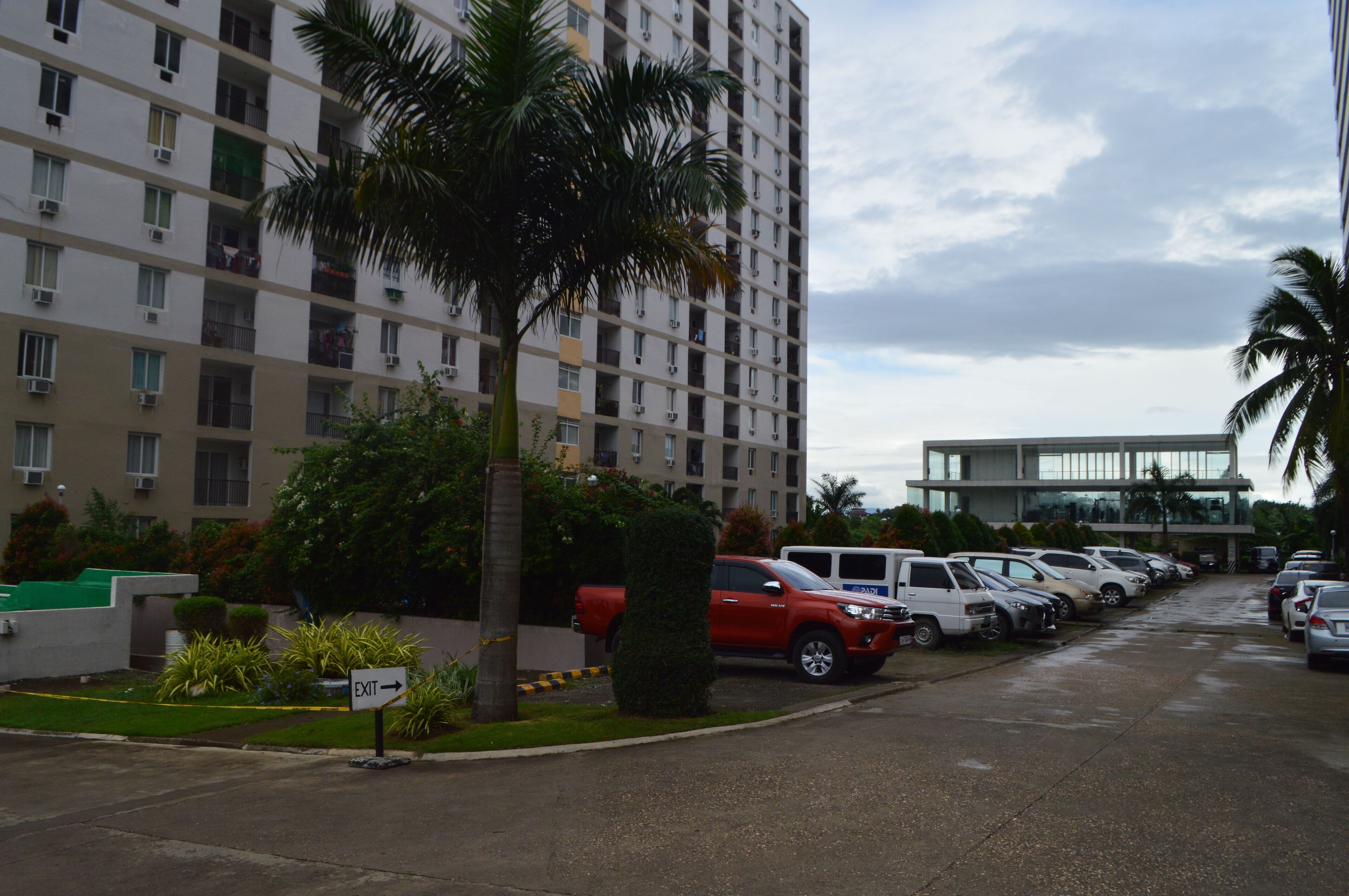Un parking avec plusieurs voitures, un véhicule rouge et un immeuble doté de balcons.