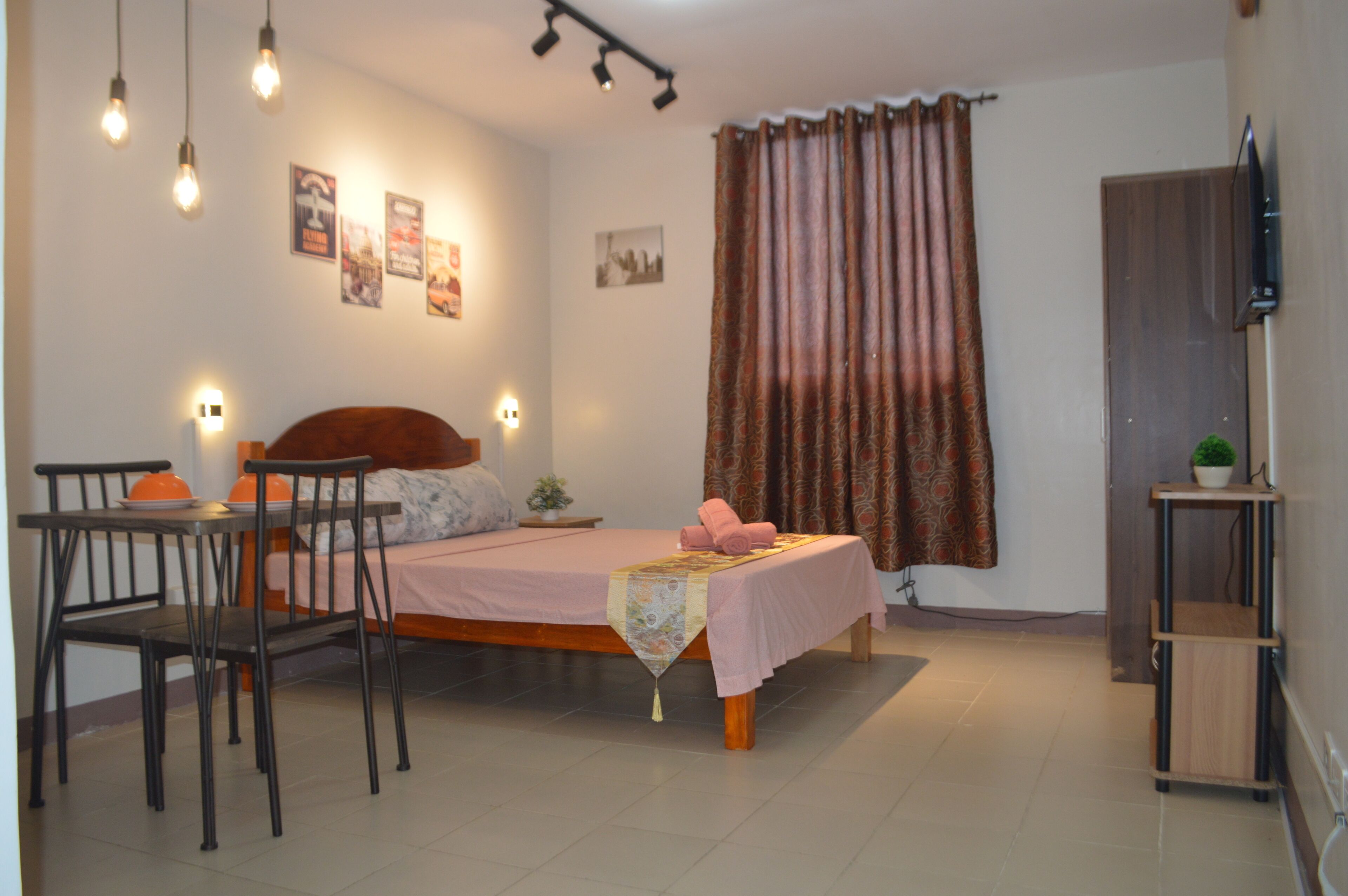 Une chambre à coucher avec un lit, une table, des chaises, un téléviseur et des rideaux.