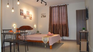 A bedroom with a bed, a table, chairs, a TV, and curtains. - Dencio's Crib (Lapu-Lapu City)
