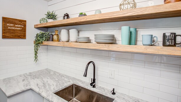 A kitchen with white subway tiles, a wooden countertop, and a sink with a faucet. There are shelves above the counter holding various kitchen items and a sign on the wall. - Fort Worth Hideaway Near Downtown (Fort Worth)