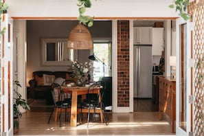 A dining area with a wooden table and chairs, a hanging light fixture, and a brick wall.