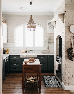 A kitchen with dark cabinets, a wooden table, a hanging light fixture, and a brick wall.