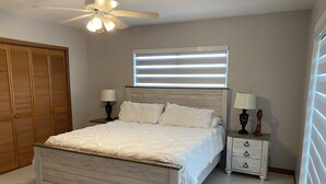 A bedroom with a wooden bed, two nightstands with lamps, a ceiling fan, and a window with blinds. - Key Largo Getaway (Key Largo)