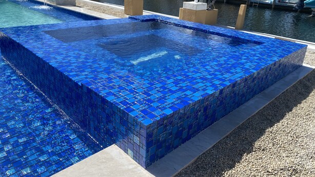 A rectangular pool with blue mosaic tiles, surrounded by a pebble beach and a water feature. - Key Largo Getaway (Key Largo)