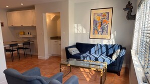 A living room with a sofa, two armchairs, a glass coffee table, a kitchen area, and a framed artwork on the wall. - Central, Quiet and Beautifully Decorated #1 (Fort Lauderdale)