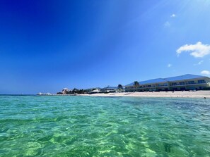 A beachfront hotel with clear blue waters, a sandy beach, and a clear sky.