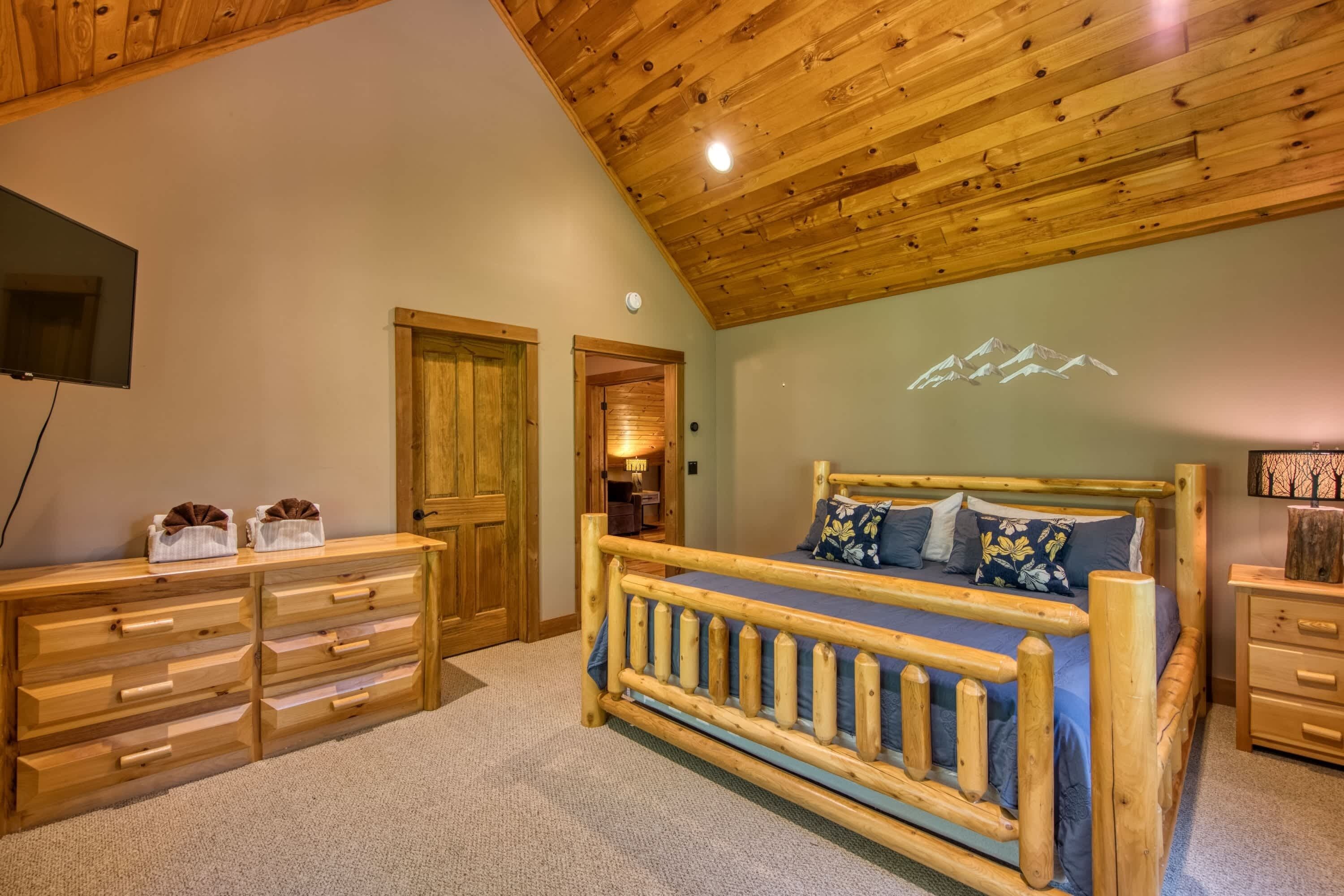 Une chambre à coucher en bois, avec un lit, une commode et un téléviseur fixé au mur.