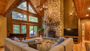 A spacious living room with a stone fireplace, a large TV, and a grand piano.
