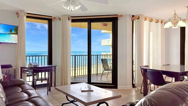 Una sala de estar con sofá de cuero, una mesa de comedor y un balcón con vista a la playa.
