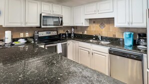 Una cocina moderna con armarios blancos, un microondas de acero inoxidable, una cafetera y un lavavajillas.