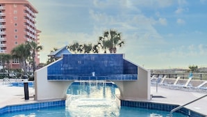 Una piscina con un puente de azulejos azules, sillas de descanso y palmeras.