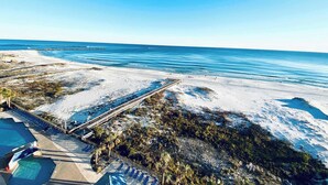 Un complejo turístico en la playa con un muelle de madera largo, piscina y sillones de descanso.