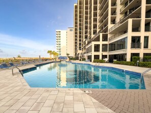 A swimming pool with lounge chairs and a building with multiple balconies in the background.