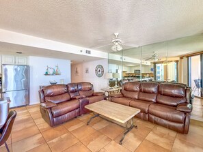 A spacious living room with a brown leather sectional sofa, a wooden coffee table, and a ceiling fan.