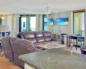 Ein modernes Wohnzimmer mit einer braunen Ledersofa, einem Esstisch mit Stühlen, einem an der Wand montierten Flachbildfernseher und einem Balkon mit Meerblick.