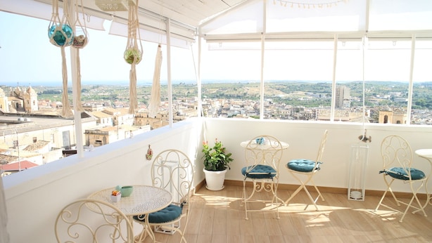 A balcony with a view of a cityscape, featuring a table and chairs, a potted plant, and hanging macramé decorations. - Noto Da Quassù Relax B&B (Noto)