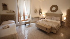 A bedroom with a large bed, a bedside table, a nightstand, a window with curtains, a chandelier, and wall decorations. - Noto Da Quassù Relax B&B (Noto)