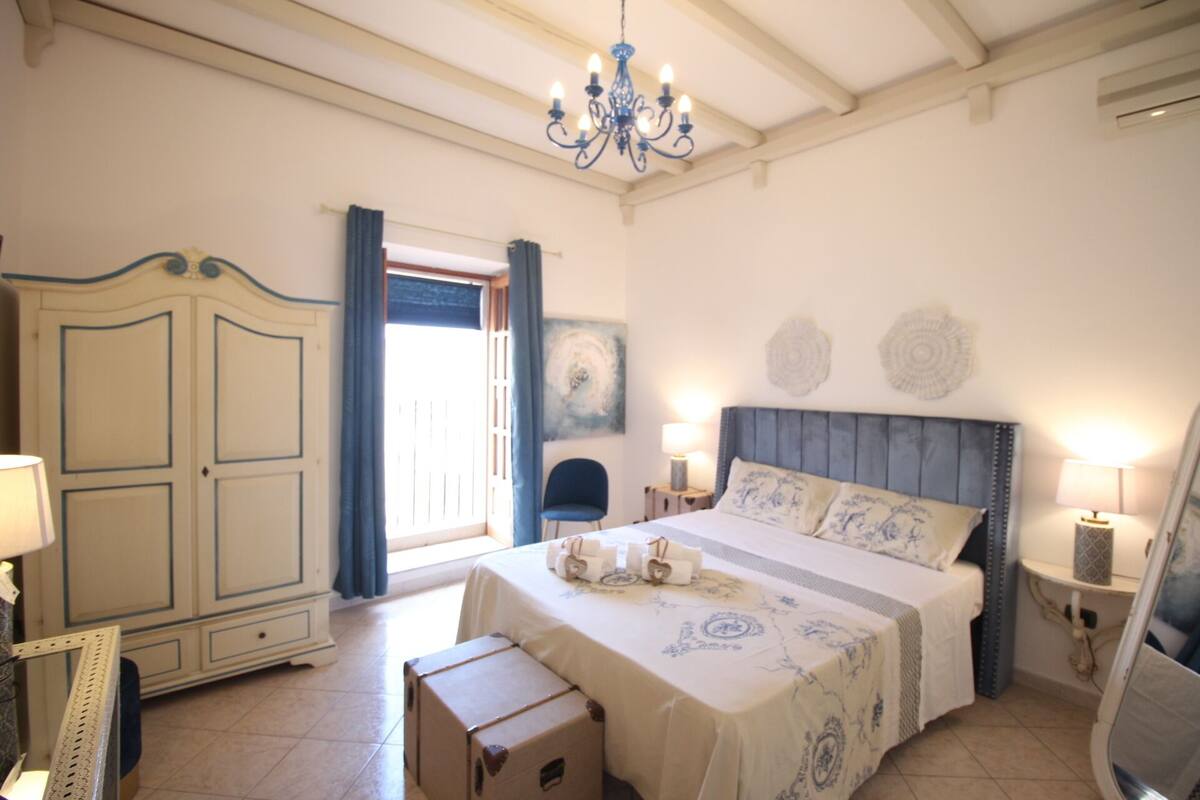 Een slaapkamer met een bed, nachtlampen, een dressoir en een kroonluchter.