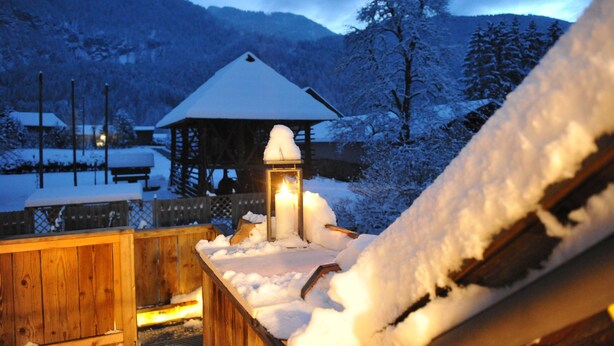 A wooden deck with a snow-covered gazebo and a lit lantern.