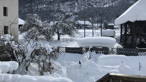 A snow-covered landscape with a wooden fence, a building, and a mountain in the background.