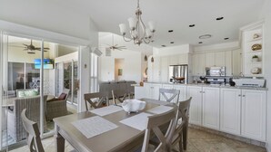 A modern kitchen with white cabinets, a dining area with a table and chairs, and a ceiling fan. - Enjoy Players Club Access in this Luxurious Naples Golf Course Home.   (Naples)