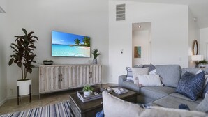 A modern living room with a large flat-screen TV, a grey sofa, and a wooden cabinet. - Enjoy Players Club Access in this Luxurious Naples Golf Course Home.   (Naples)