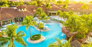 Un complexe hôtelier doté d’une piscine centrale, de palmiers et d’espaces de détente.