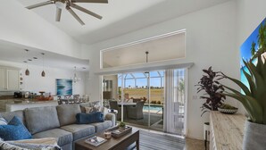 A spacious living room with a large sofa, a coffee table, and a dining area with chairs. There is a sliding glass door leading to a patio with a view of a golf course and a pool. - Enjoy Players Club Access in this Luxurious Naples Golf Course Home.   (Naples)