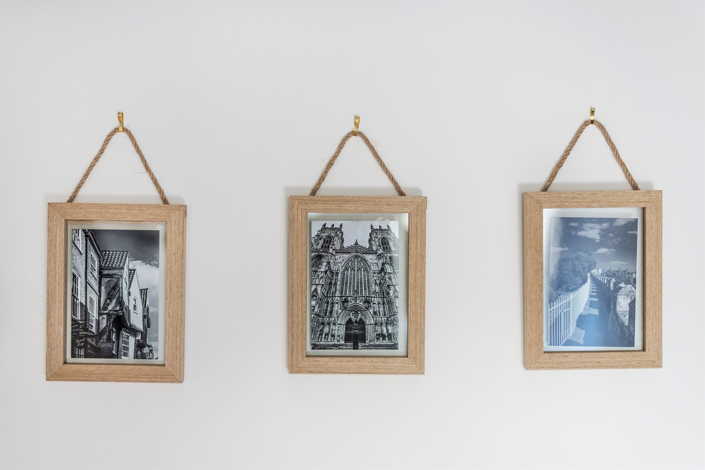 Three framed black and white photographs of buildings, each hanging on a wall with a simple rope.