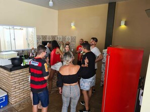 Eine Gruppe von Personen in einer Küche mit einer Ziegel-Arbeitsplatte, einem roten Kühlschrank und einer gefliesten Spritzwand.