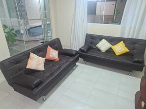 Zwei schwarze Ledersofas mit Kissen, eine Glastür und ein Blick ins Freie.