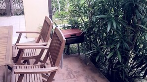 Un espacio al aire libre con patio, mesa y sillas de madera, rodeado de follaje denso.