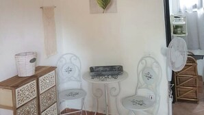 Una habitación con una mesa, dos sillas, una lámpara colgante, una hoja decorativa y un ventilador de pared.