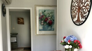 A hallway with a wooden floor, a patterned rug, a table with a vase of flowers, a framed painting, and a wall-mounted tree decoration. - Spacious & gracious (Hamilton)