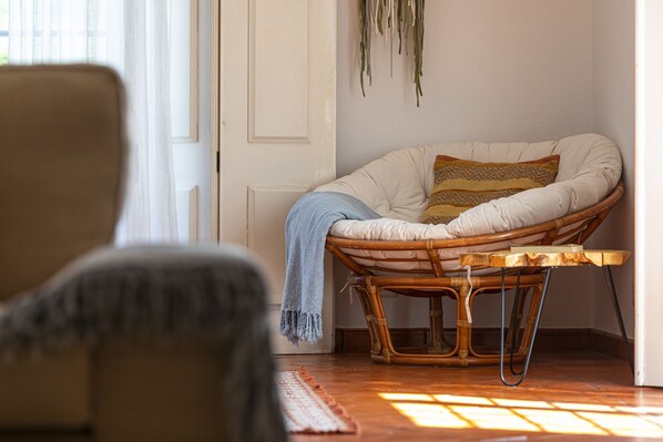 A room with a wicker chair, a wooden table, and a patterned cushion.